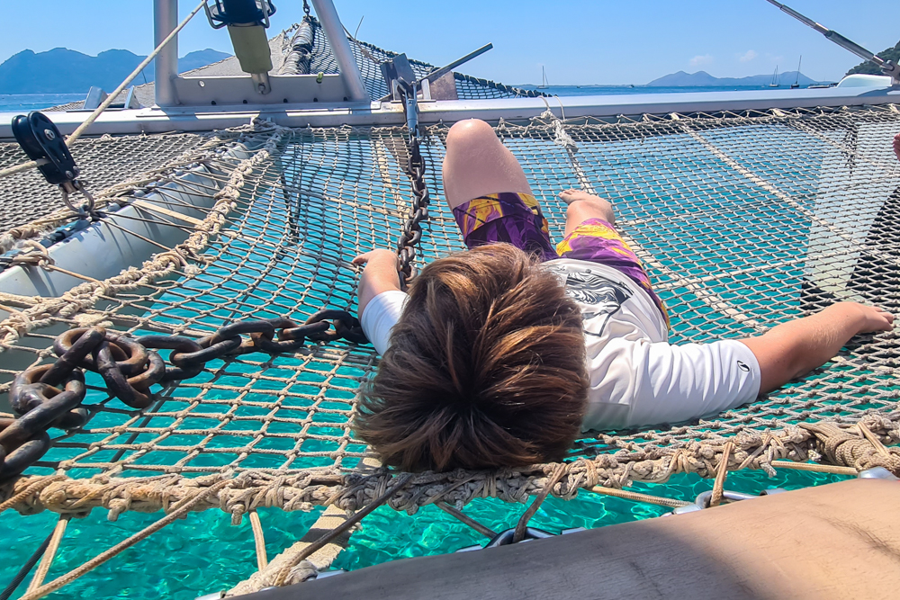 Kind liegt auf dem Netz am Bug während einer Katamaran-Tour auf Mallorca