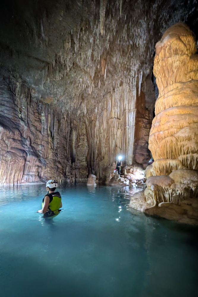 Kind steht in der Cova des Coloms Höhlentour im türkisblauen Wasser einer Tropfsteinhöhle auf Mallorca