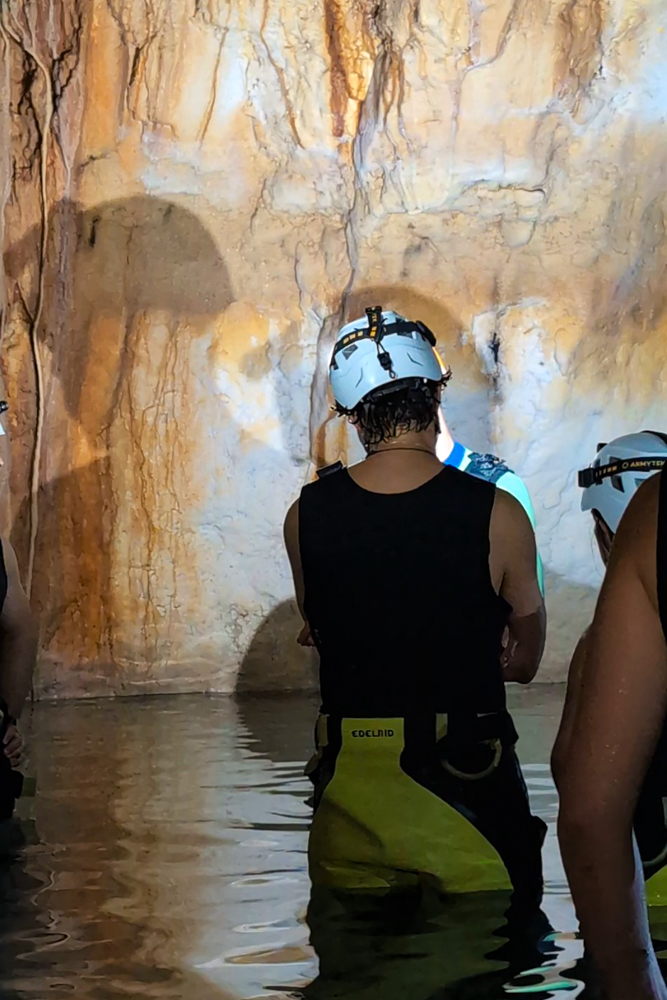 Teilnehmer der Cova des Coloms Tour erkunden die überflutete Höhle mit Helmen und Neoprenausrüstung