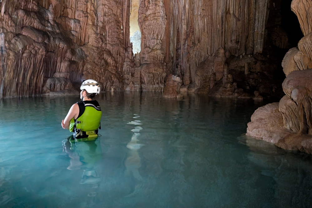 Kind steht in der Cova des Coloms Höhlentour im türkisblauen Wasser einer Tropfsteinhöhle auf Mallorca