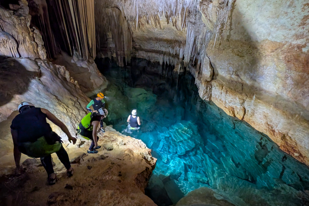 Blick auf das türkisfarbene Wasserbecken der Cova des Coloms mit Teilnehmern beim Erkunden der Höhle