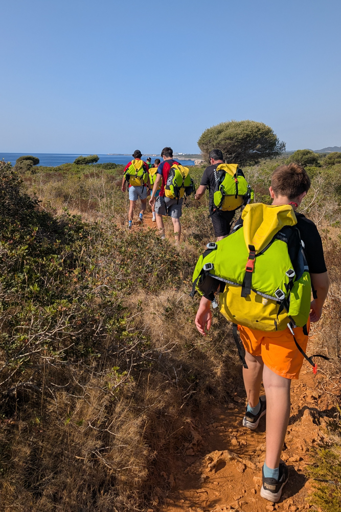Teilnehmer der Cova des Coloms Tour wandern mit Ausrüstung durch die Küstenlandschaft Mallorcas